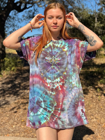 Person wearing a tie-dye t-shirt with a dragonfly design outdoors.